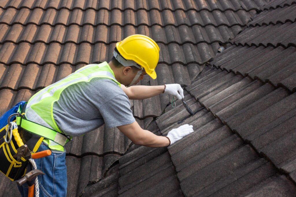 Worker man using waterproof roof coating repair to fix crack of the old tile roof